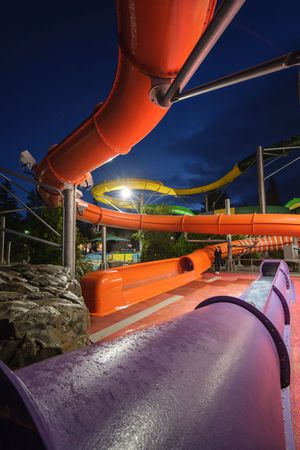 Colorful water park slides illuminated at night with vibrant orange, yellow, and purple tubes against a dark blue sky.