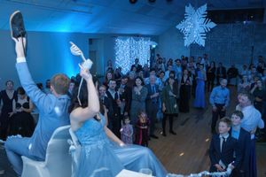 Couples dance at a winter wonderland themed formal event with snowflake decorations and a crowd of guests.