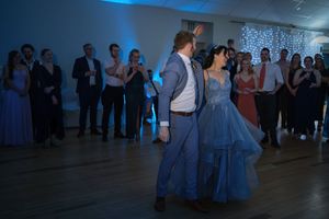 Couple shares first dance in blue formal wear at elegant prom or wedding reception with guests watching.
