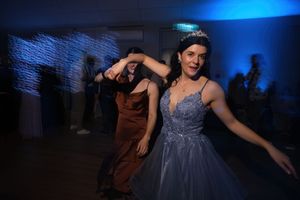 Woman in blue ball gown and tiara dancing at a formal event with blue lighting.