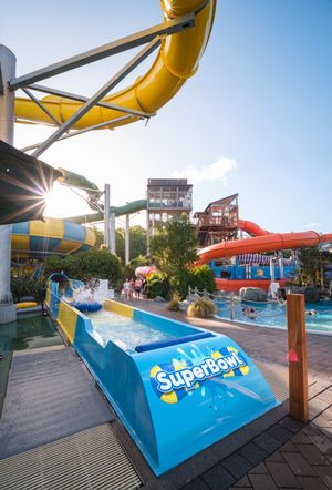 SuperBowl water slide attraction at a vibrant outdoor waterpark on a sunny day with colorful slides in background.