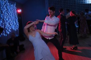 Couple dancing together at a formal party with festive string lights in background.