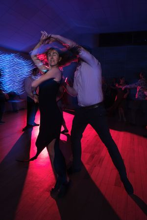 Couple performing energetic Latin dance under dramatic red and blue lights on a crowded dance floor.