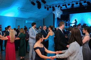 Guests holding hands and dancing in a circle at an elegant wedding reception with blue ambient lighting.