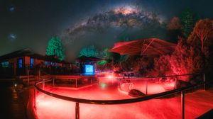 Night sky observatory with Milky Way galaxy visible above red-lit viewing platform surrounded by trees.