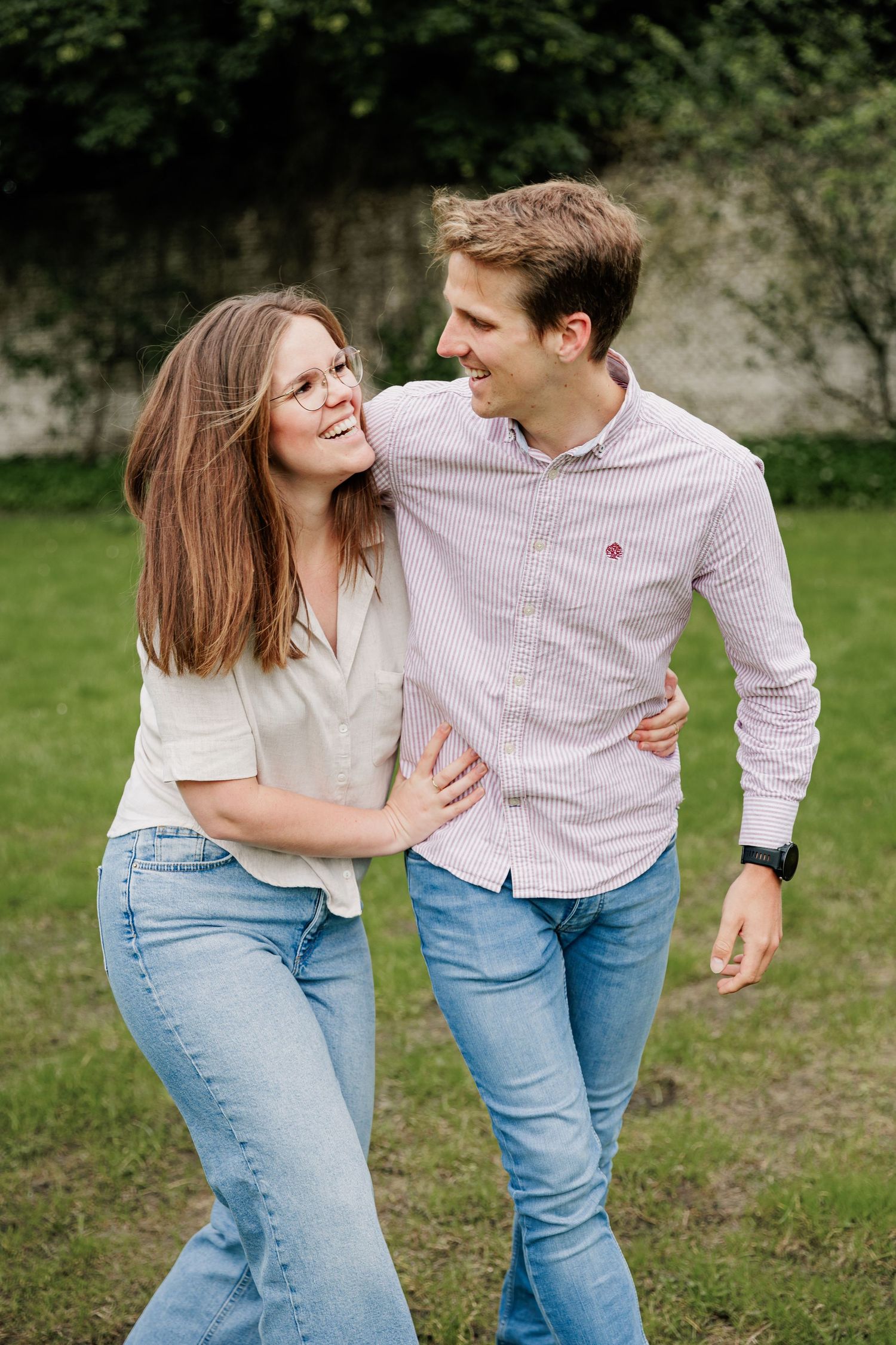 Playful couple in casual attire laughs together during outdoor photo session.