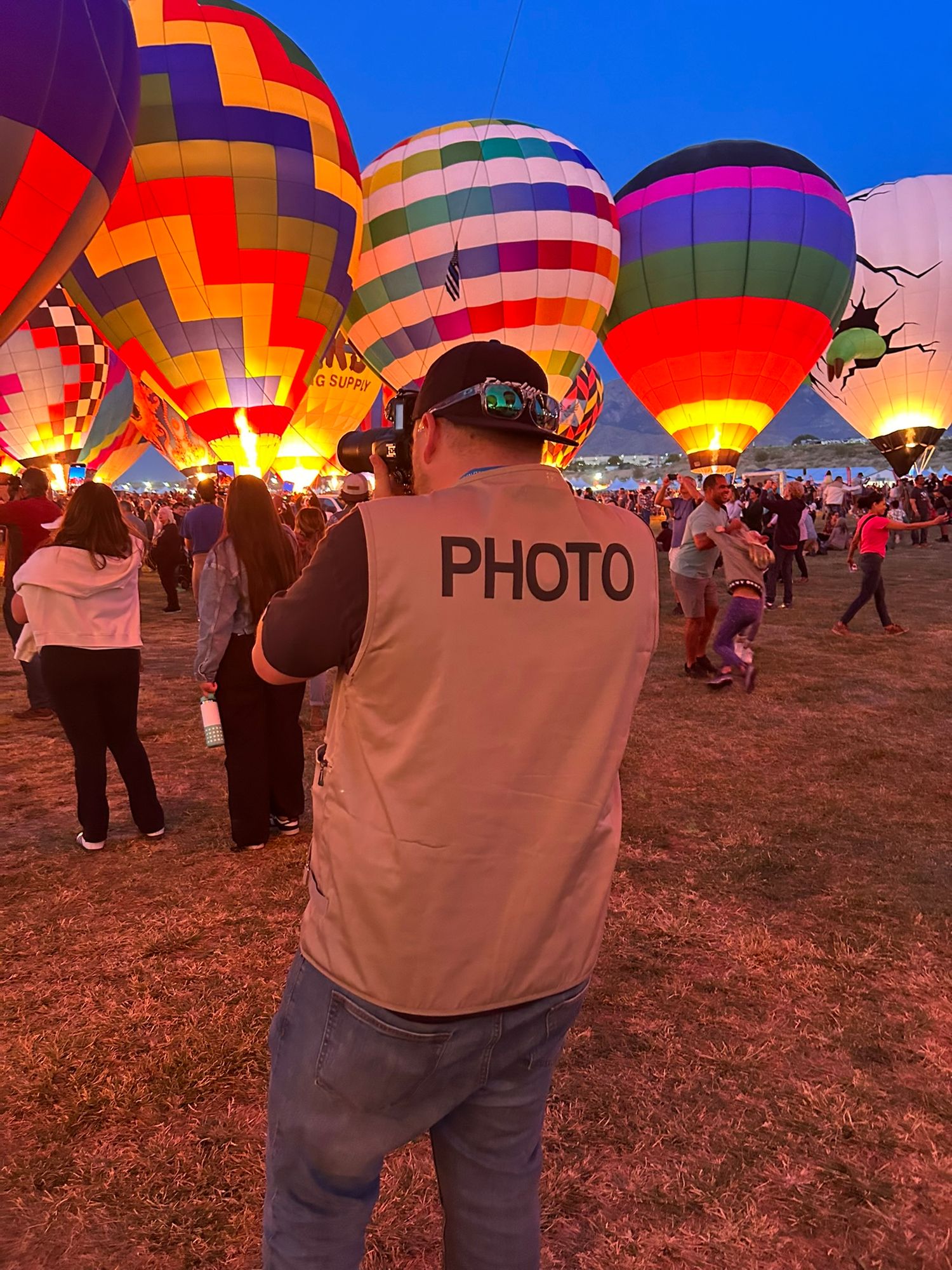 Photographer in PHOTO vest shooting hot air balloons at dusk festival.