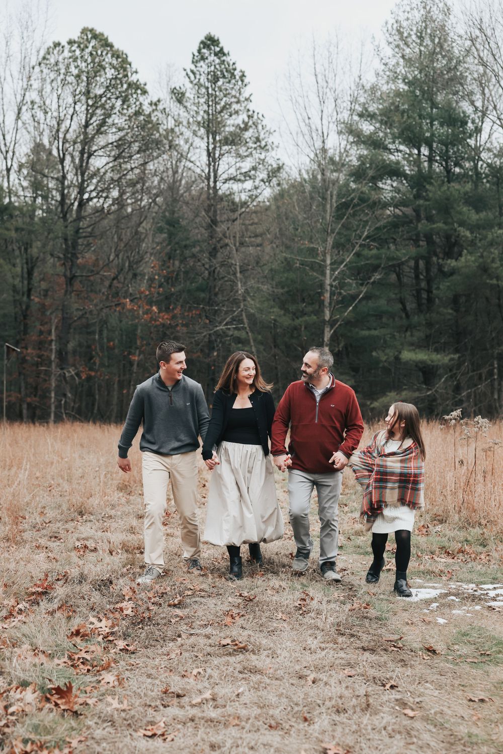 Family walking together through a rustic autumn field with tall grass and trees in the background.