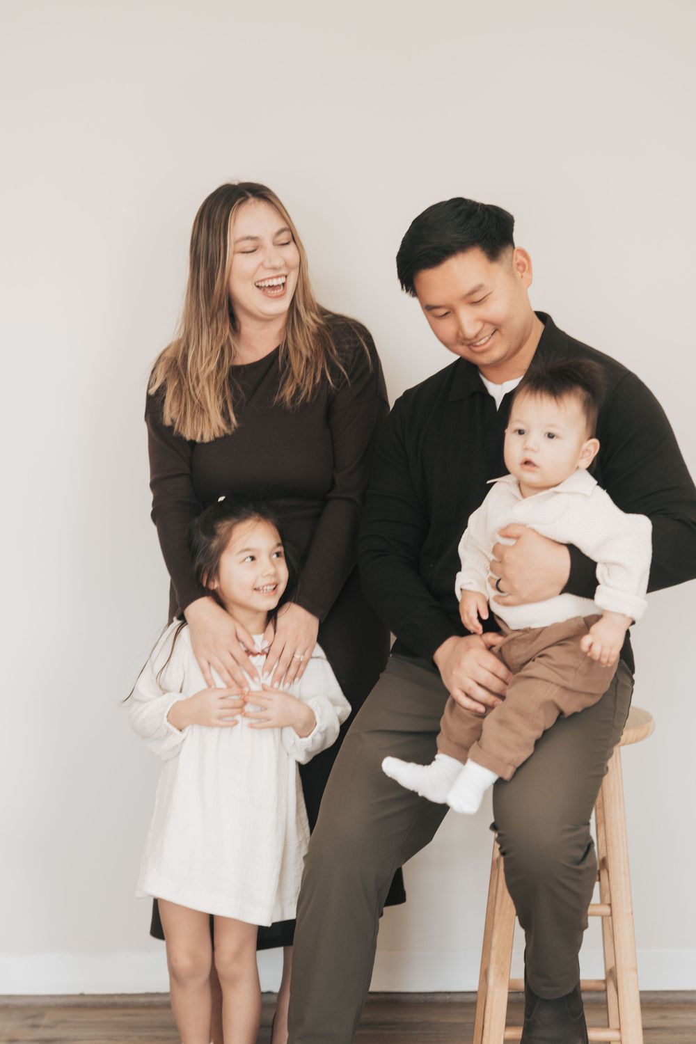 Happy family portrait with parents and two young children posing together against a white background.