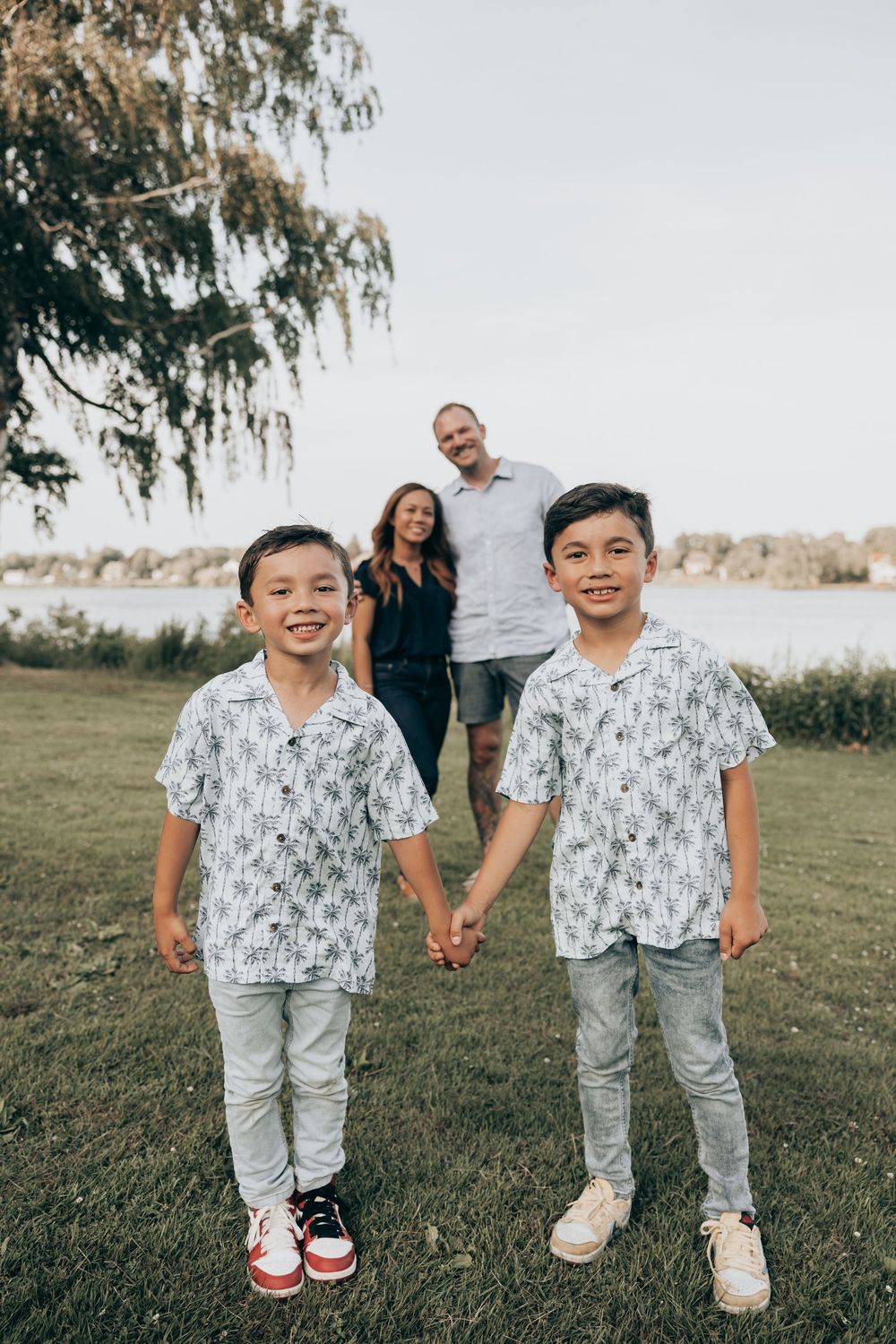 Two children wearing matching patterned outfits stand together on grassy lawn at sunset.