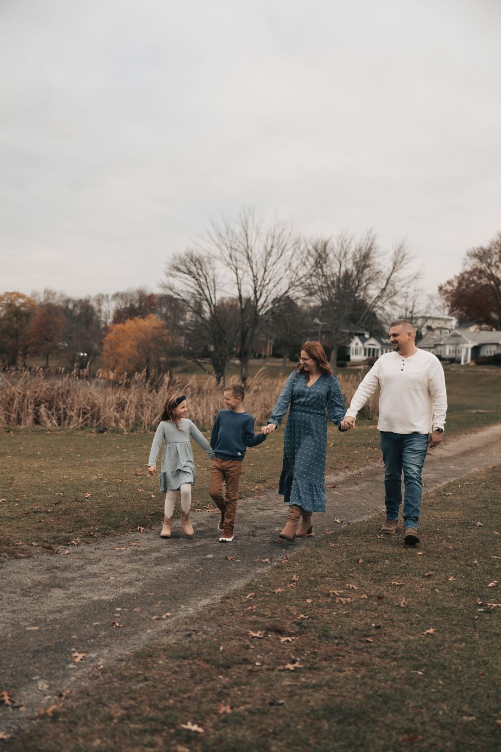 A group of people walk together on a dirt path through an autumn field on an overcast day.