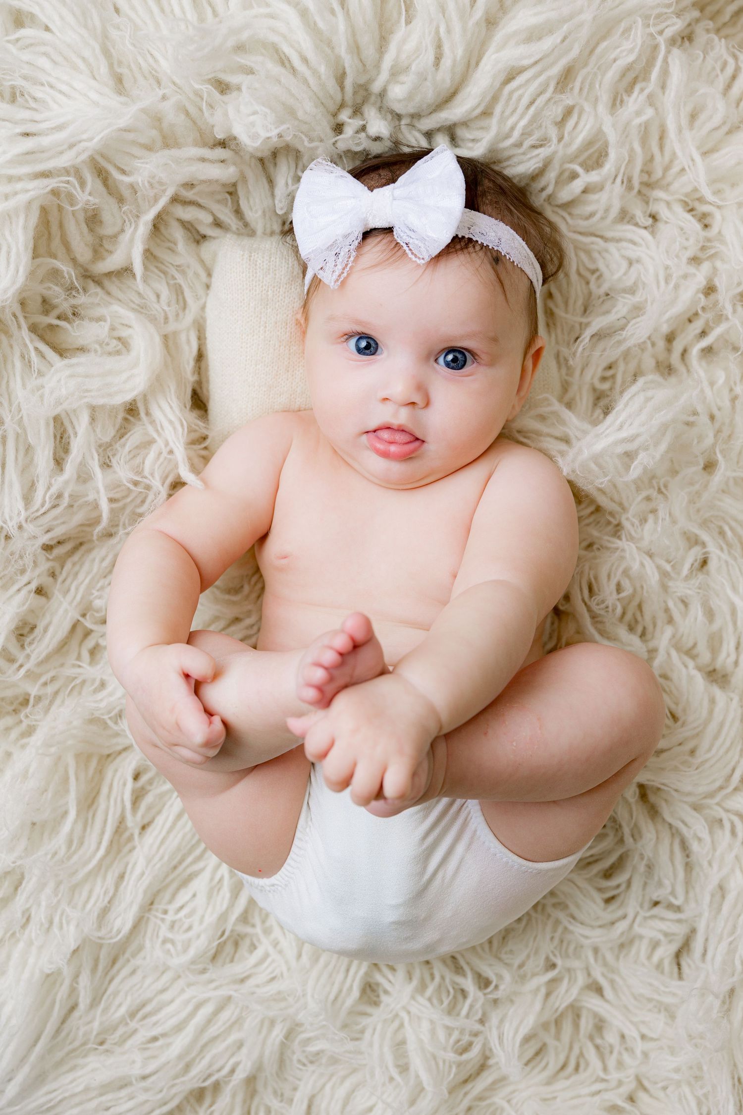Adorable Indian baby with dark curly hair and brown eyes wearing a white sleeveless outfit, looking sideways.
