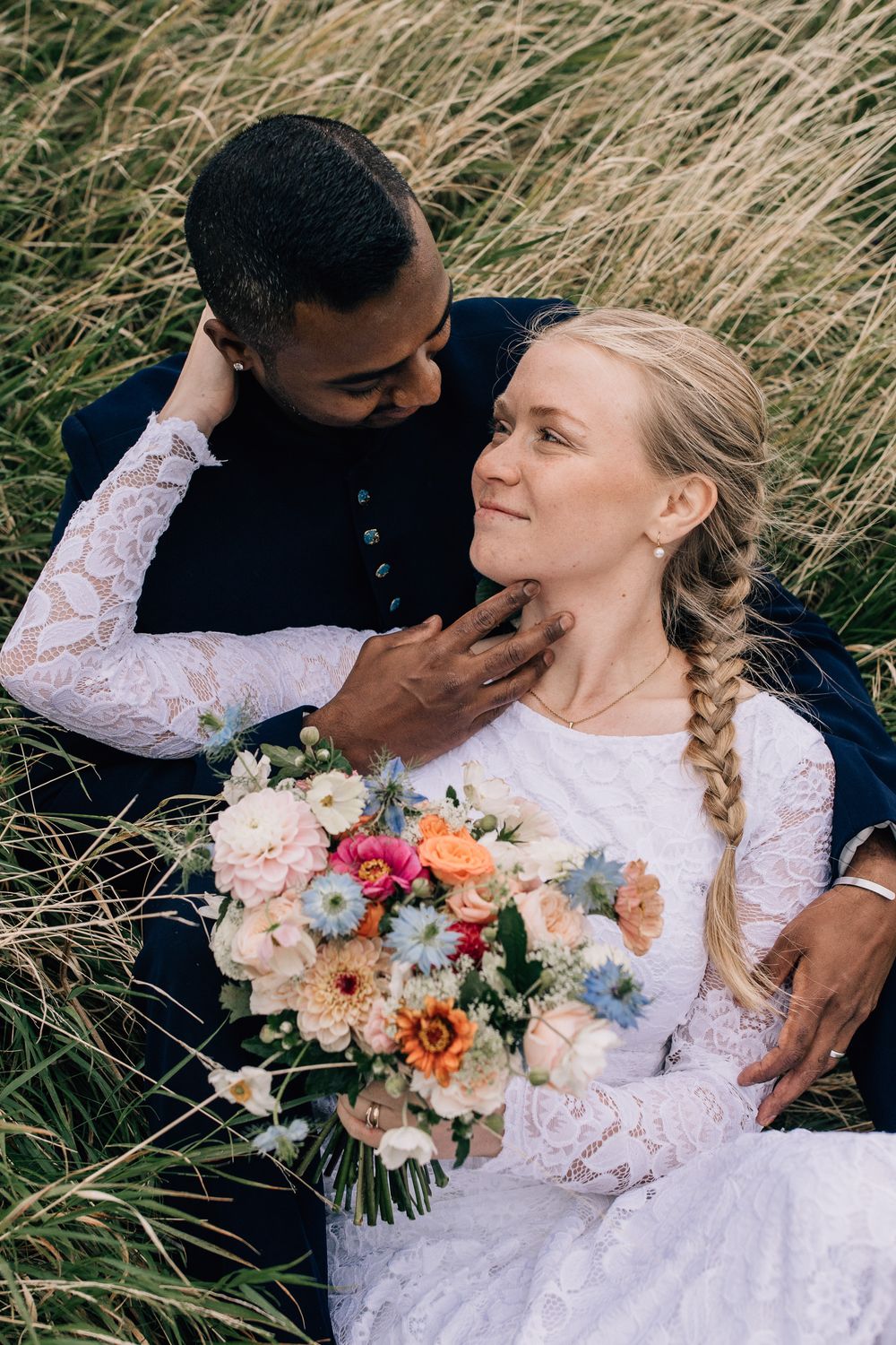 Brudpar myser i gräset under deras bröllopsfotografering på varbergs fästning