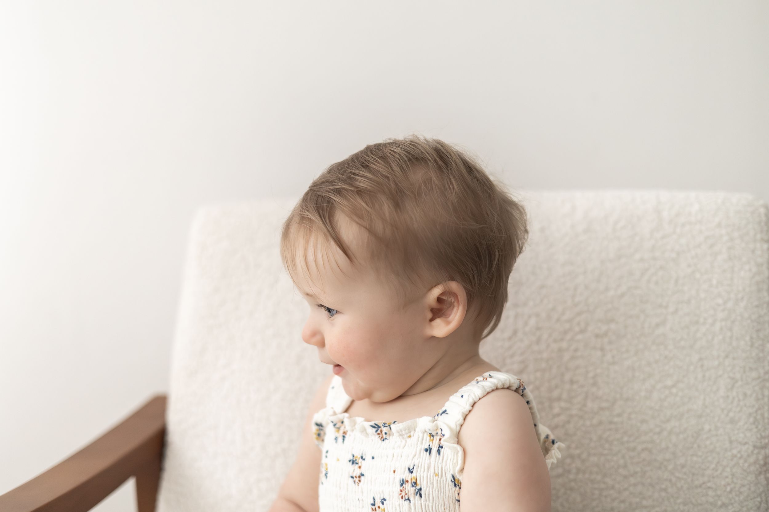 Adorable baby in floral romper sitting in a white chair, baby birthday photoshoot Nottingham natural relaxed