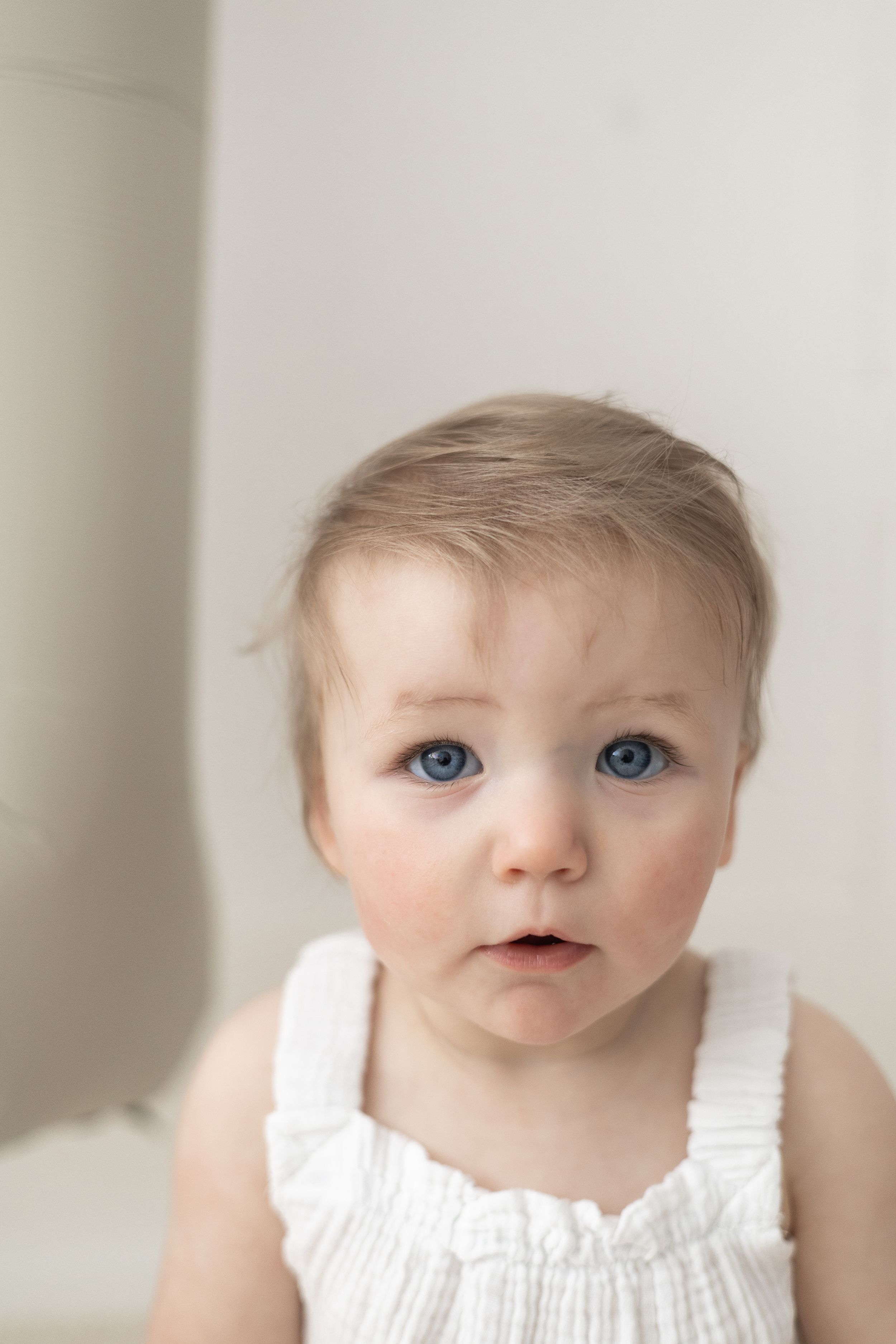 Adorable baby with blue eyes and light hair wearing a white sleeveless outfit baby birthday Nottingham photoshoot natural relaxed
