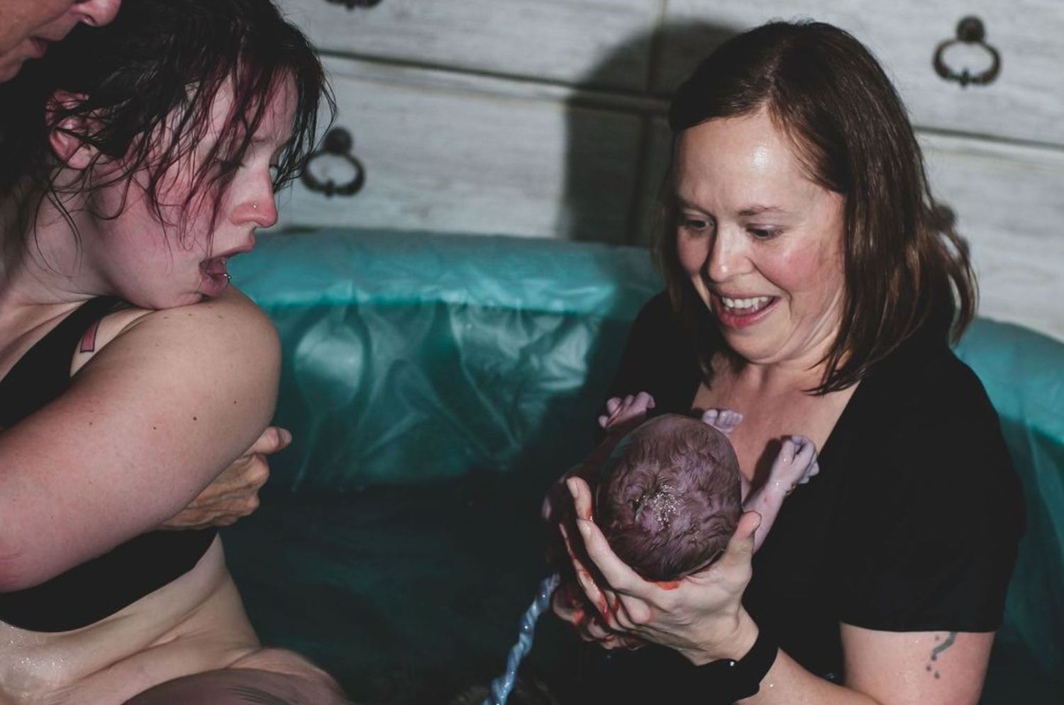 Joyful moment during water birth as newborn baby is held in birthing pool.