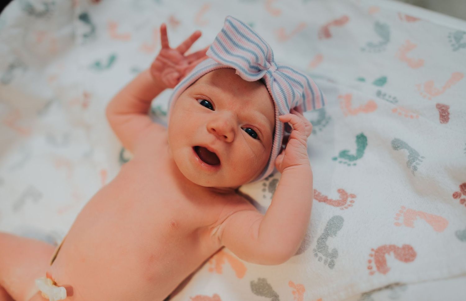 Happy baby wearing a gray bow lies on a colorful patterned blanket.