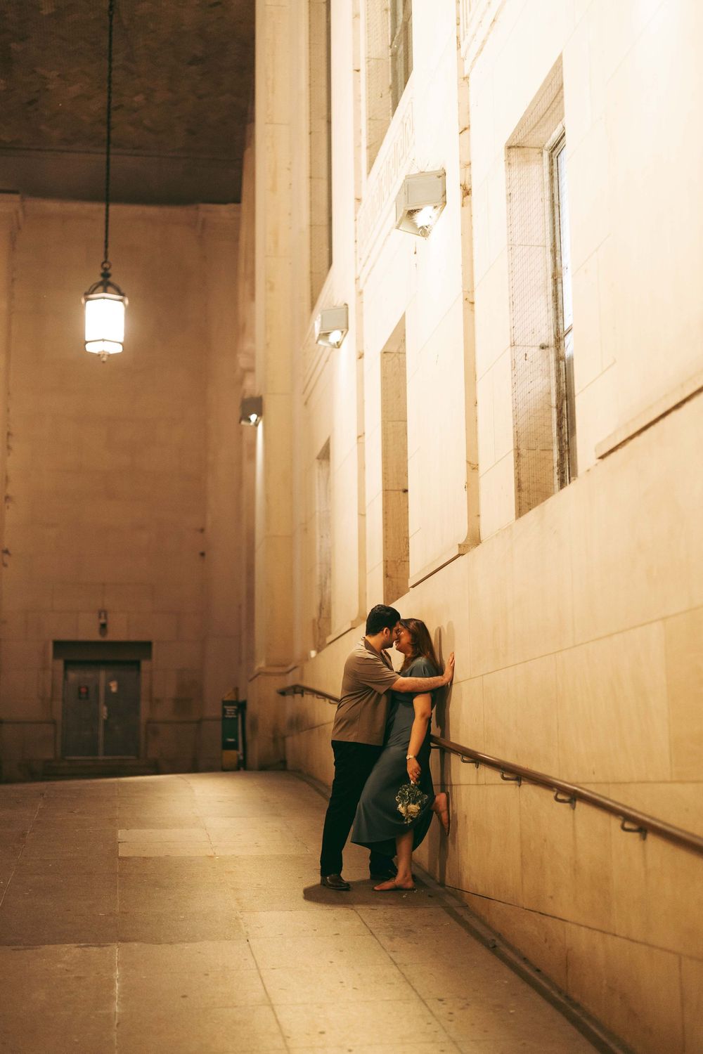 Couple sharing a romantic moment leaning against a wall in a grand building corridor at night.