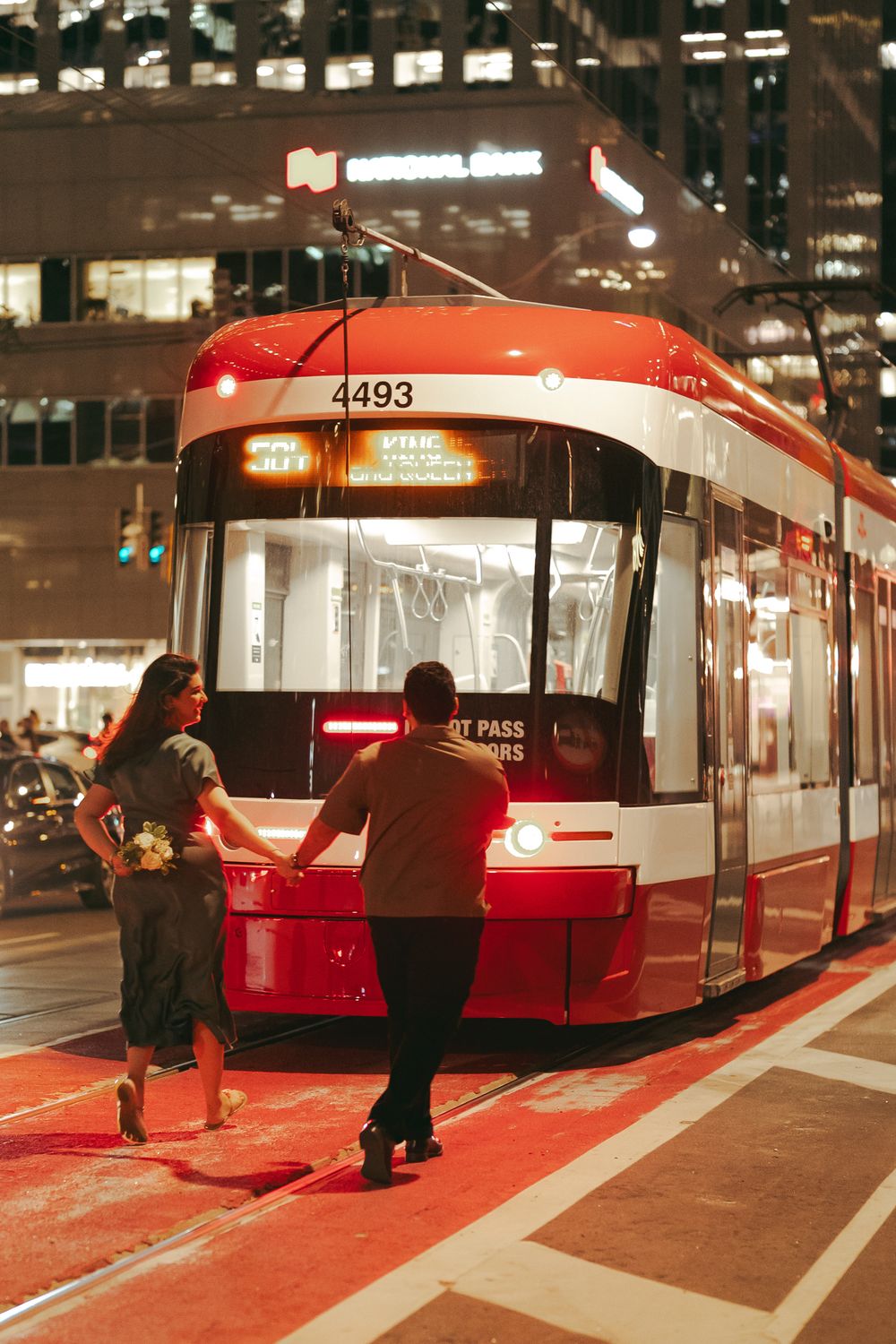 Couple holding hands boarding a red TTC streetcar number 4493 at night in downtown Toronto.