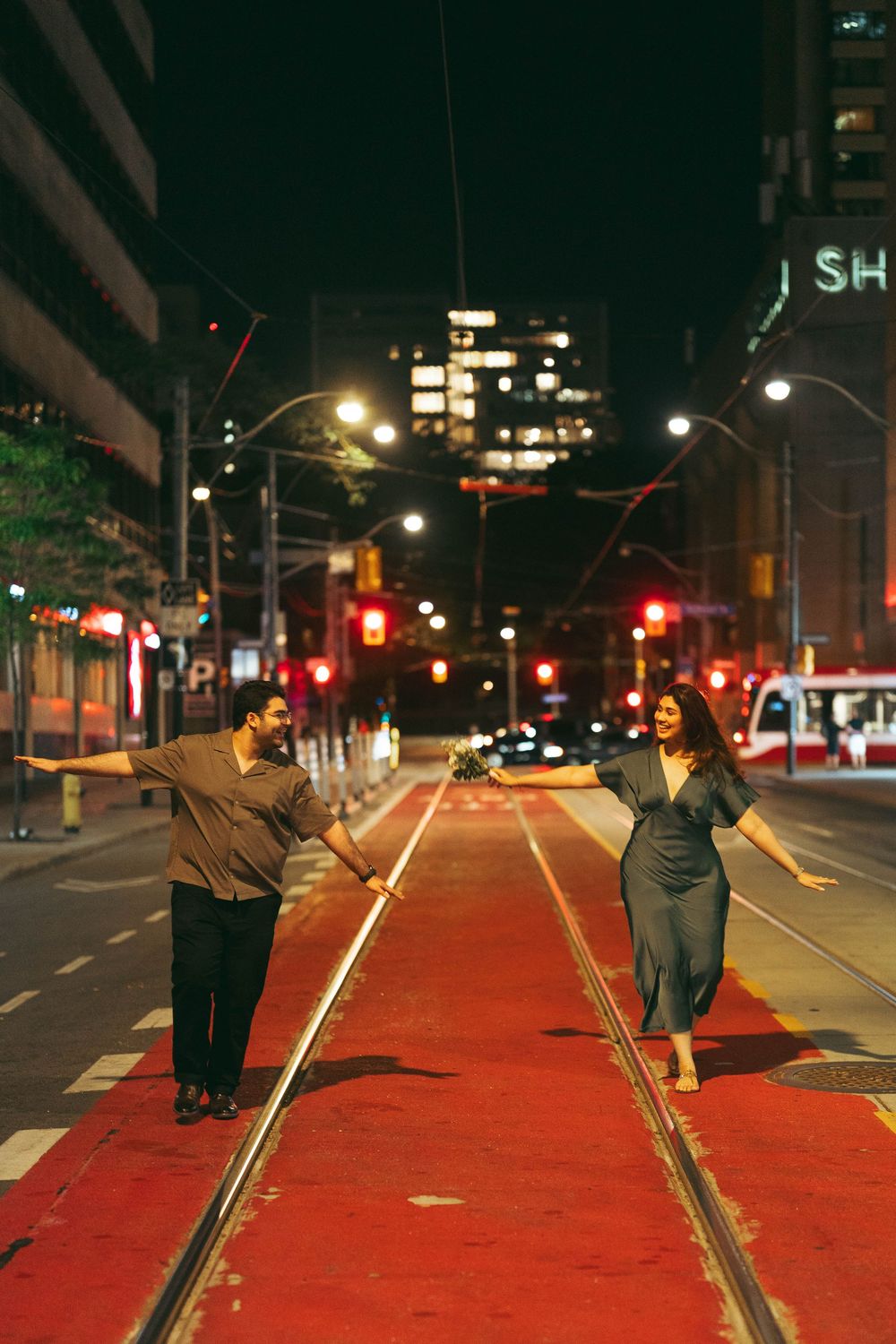 Couple posing on red streetcar tracks at night on a Toronto city street with traffic lights.