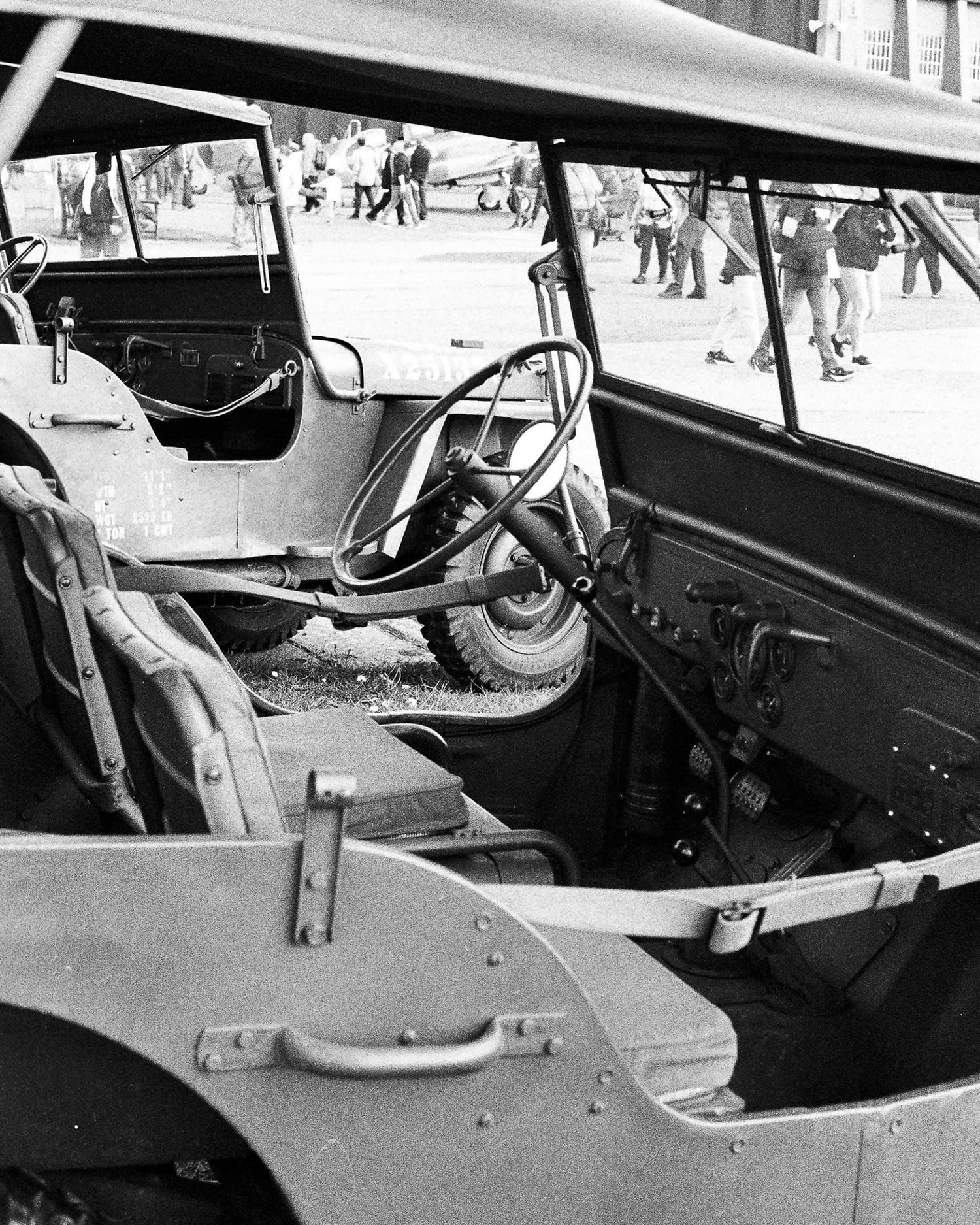 Black and white photo showing the interior of a vintage military Jeep with steering wheel visible at an outdoor event.