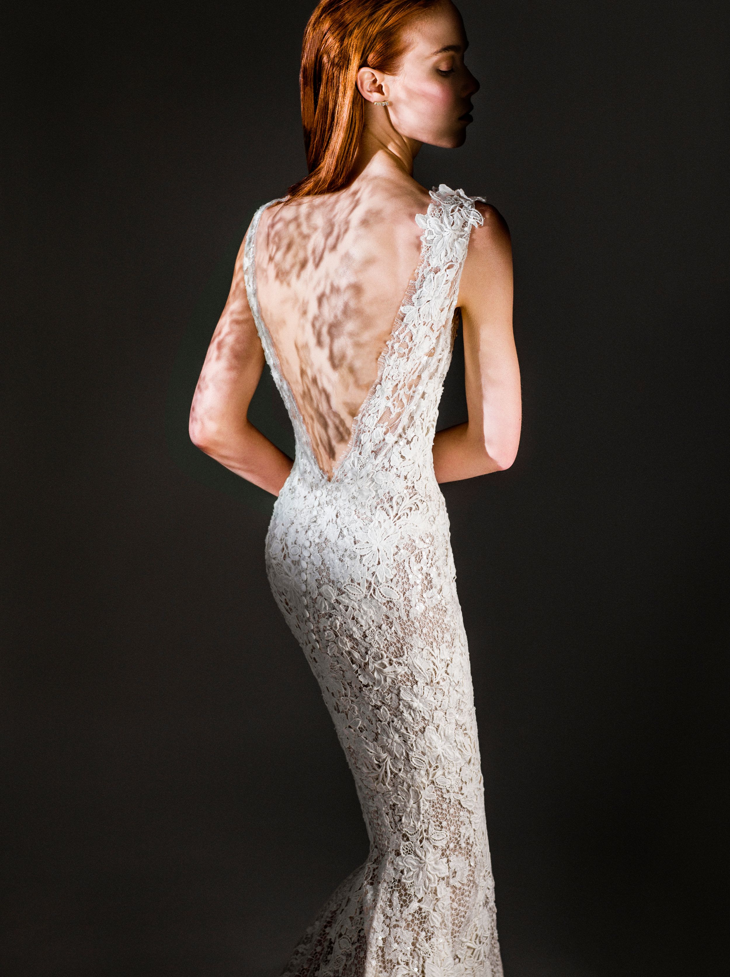 Elegant backless lace wedding gown with deep V-back and fitted silhouette on a redhead model.