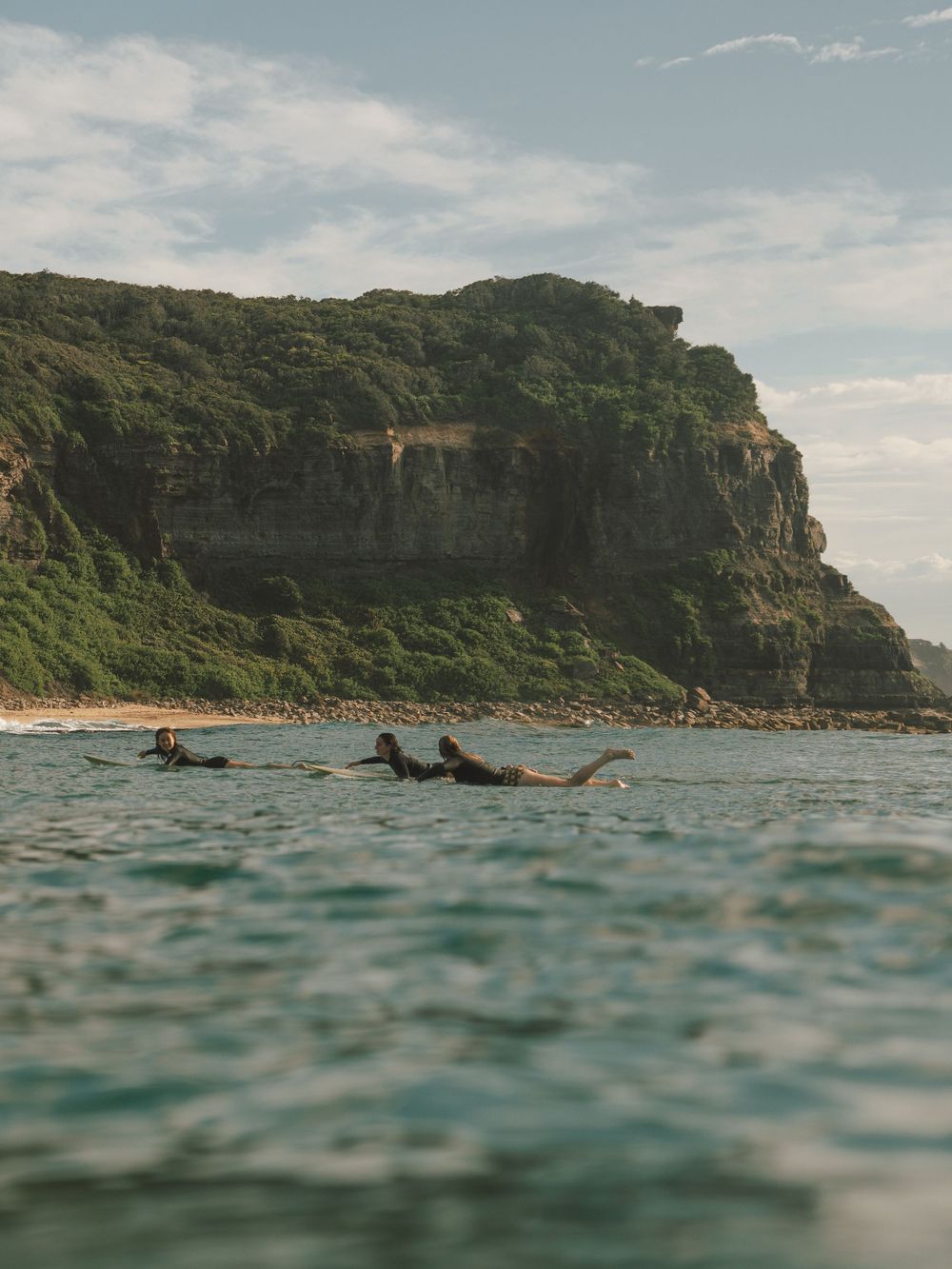 three female surfers with Dudley cliffs in background with Sunlight Surfers social surf Newcastle NSW