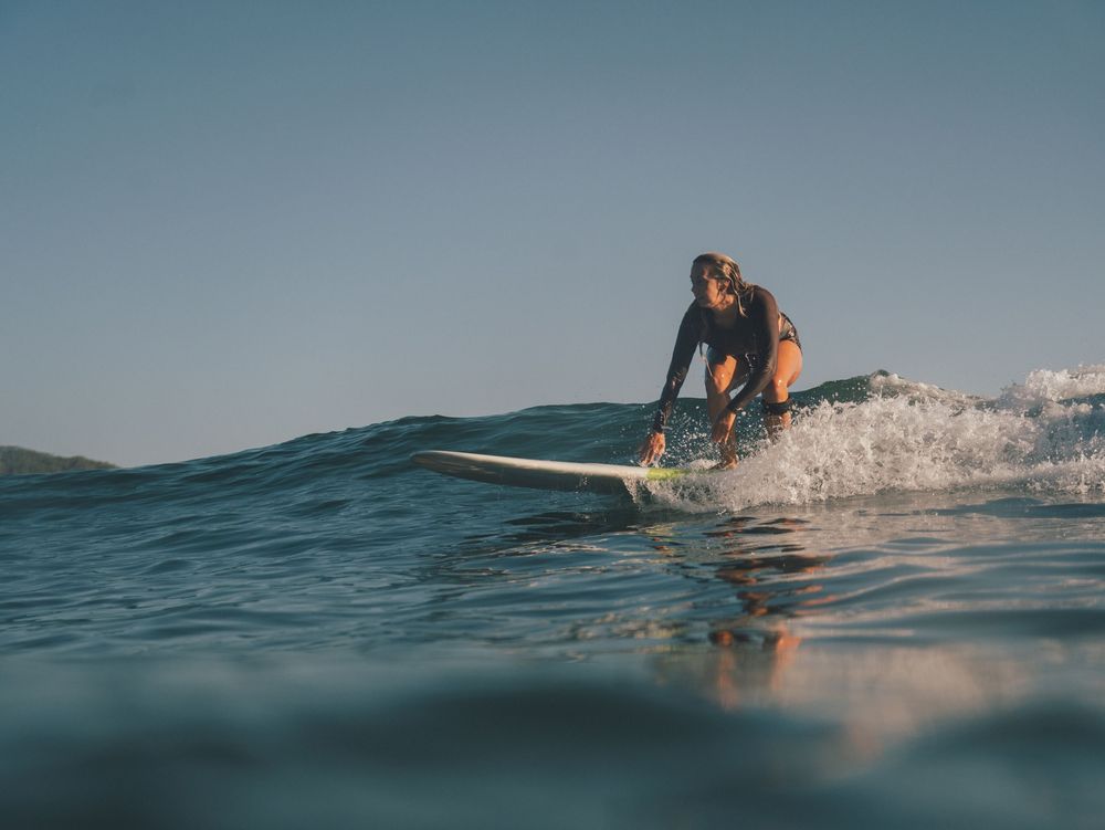 female surfer taking off on a small wave with her reflection on the wave below at Seal Rocks NSW near Newcastle