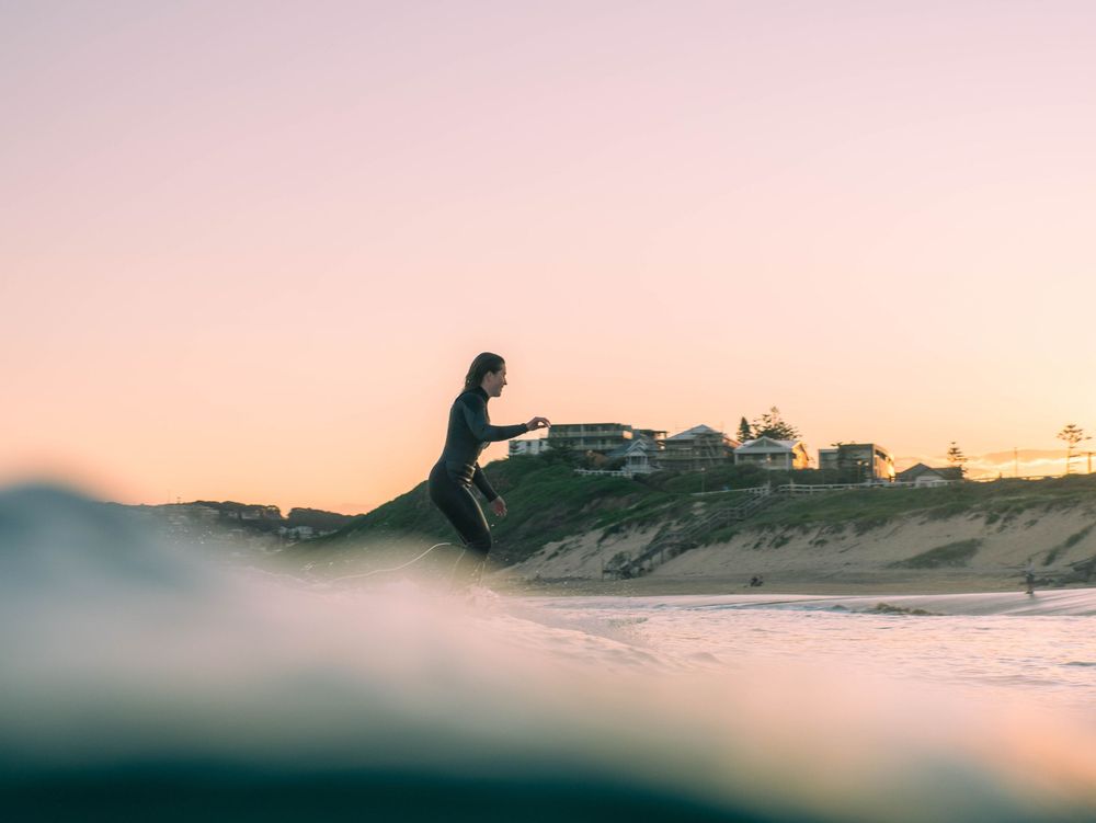 Photo of woman surfer at Bar Beach Newcastle NSW with soft after sunset glow over the waves