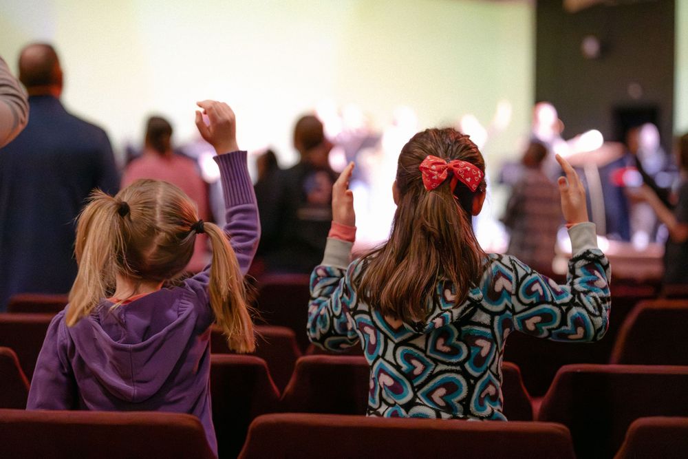 Two young girls raising their hands in worship during a church service.