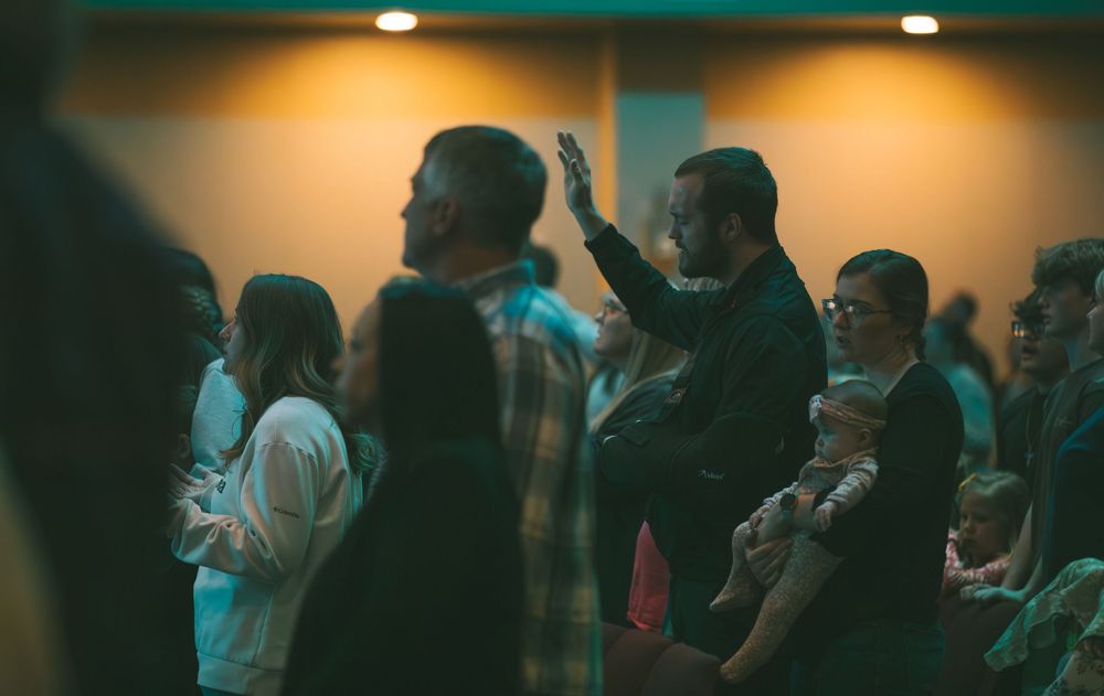 Congregation members raising hands in worship during a dimly lit church service.