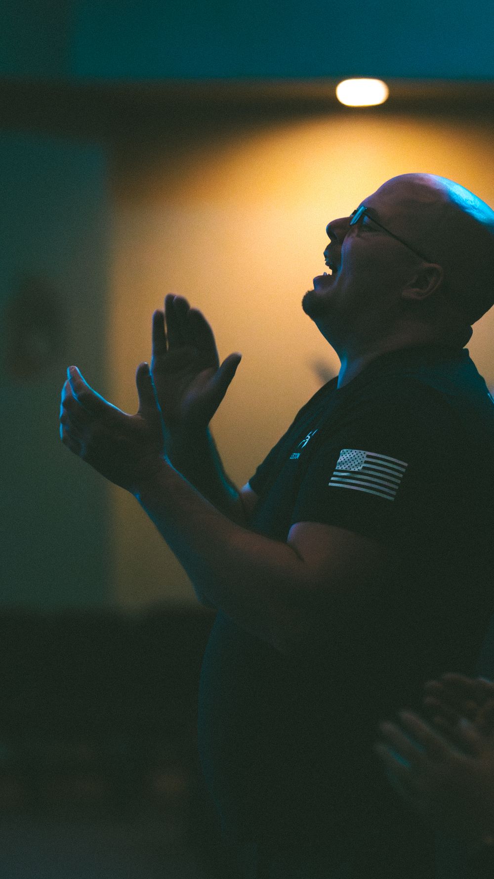 Bald man with glasses raising hands in prayer during a church worship service.
