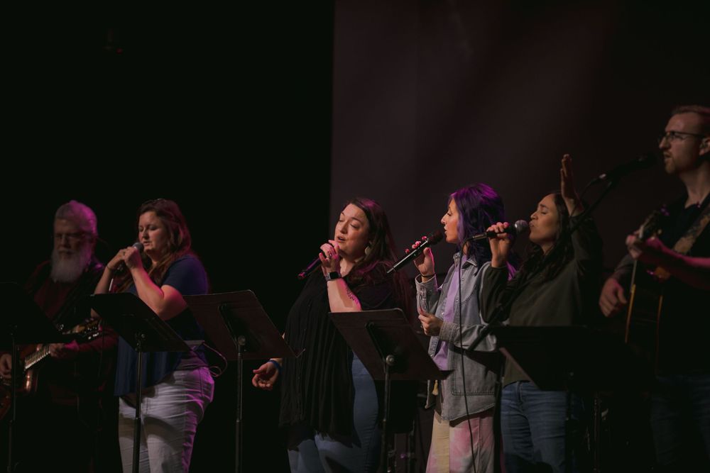 Diverse worship team singing on stage with microphones during a church service.
