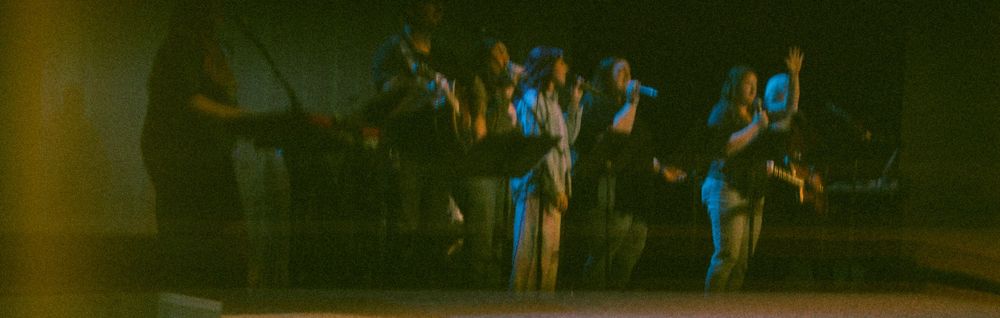 Worship band performing together on a dimly lit stage during a church service.