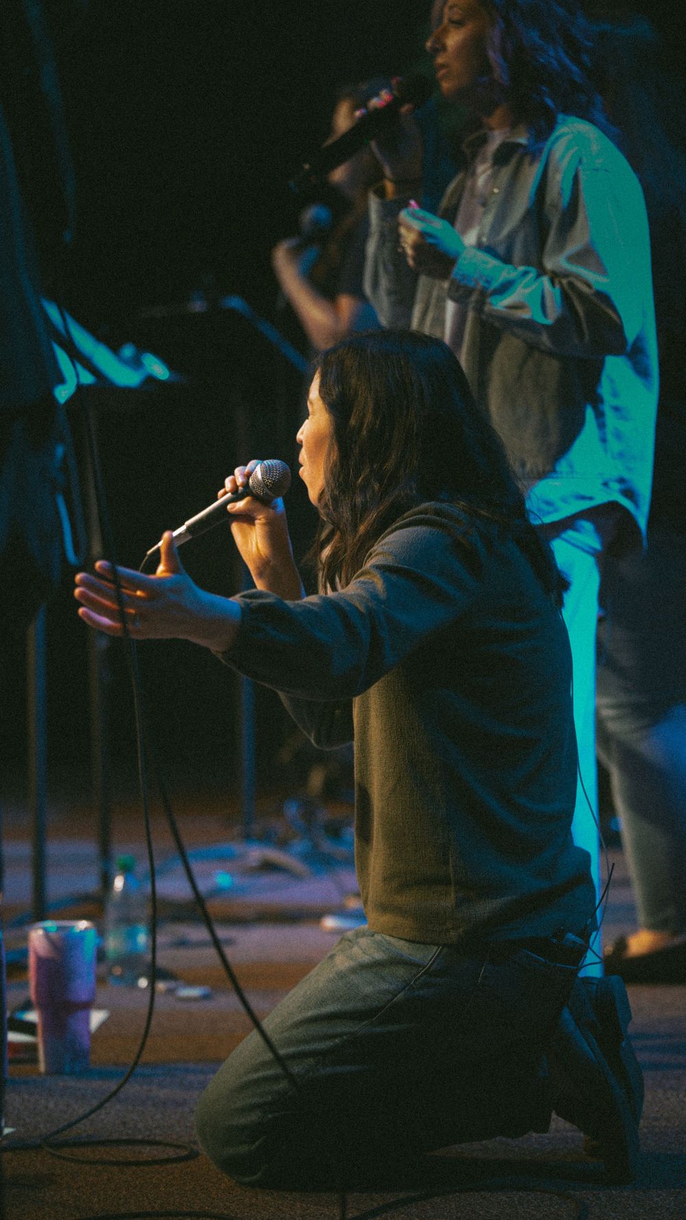 A female vocalist kneels on stage holding a microphone during an emotional church worship performance.