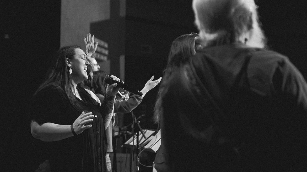 Two female worship singers perform passionately at microphone stands in a black and white church photo.