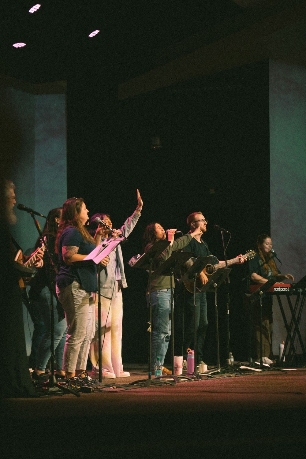 Worship band performs on stage with singers raising hands during a church service.
