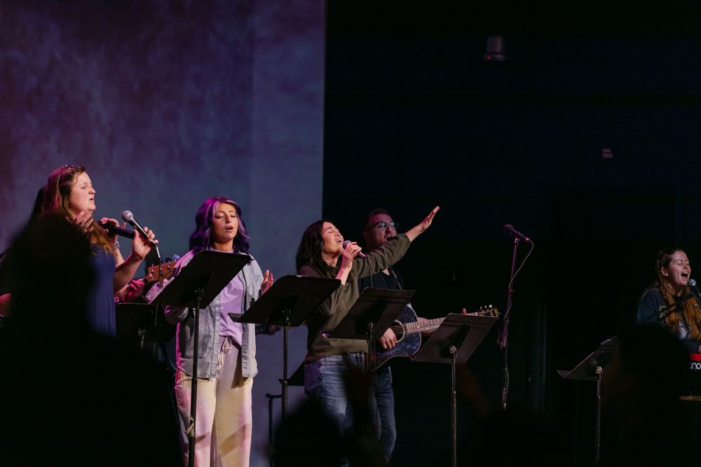 Worship team singers perform on stage with microphones during a church music service.