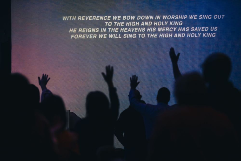 Congregation raises hands in worship with projected lyrics about the High and Holy King.