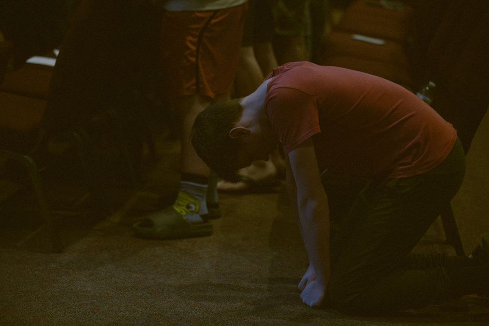 Young man kneeling in prayer on the floor during a Christian worship service.