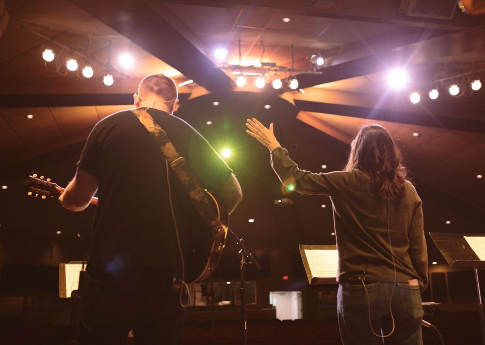 Two musicians performing on stage with bright concert lighting from above.