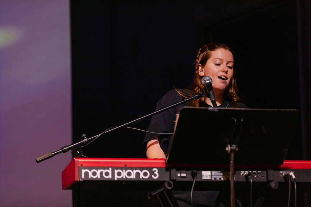Young woman singing and playing a Nord Piano 3 keyboard on stage.