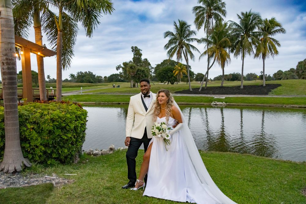 Bride and groom pose together near a pond surrounded by palm trees at outdoor wedding venue.