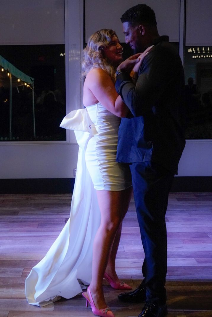 Bride in short white dress with train and groom in dark suit sharing first dance at wedding reception.