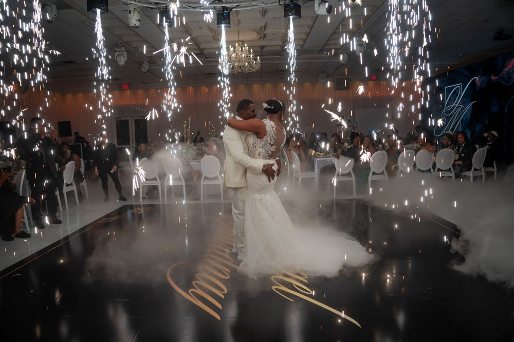 Bride and groom share first dance surrounded by fireworks and fog at elegant wedding reception.