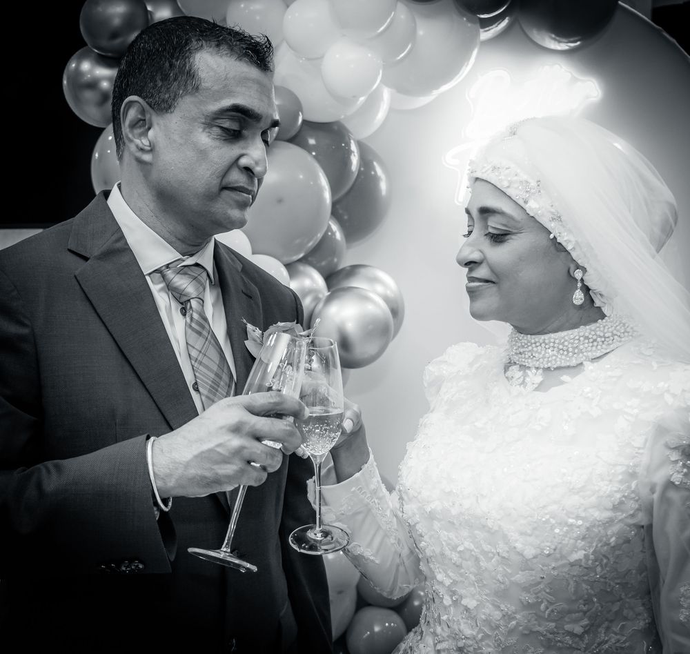 Black and white photo of bride and groom toasting with champagne glasses at wedding celebration.