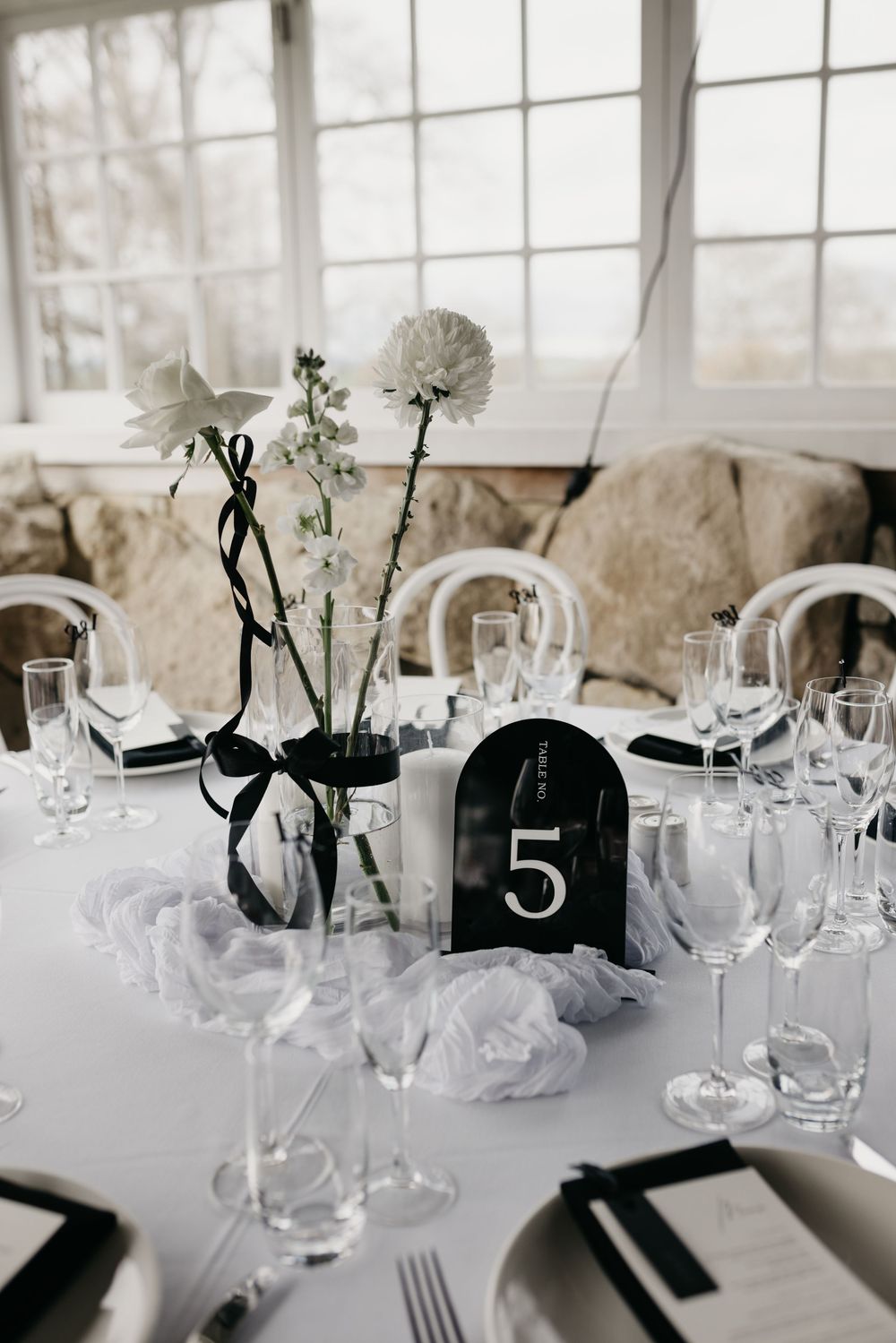Elegant wedding reception table setting with white florals, black ribbon accents, crystal glassware, and black table number five.