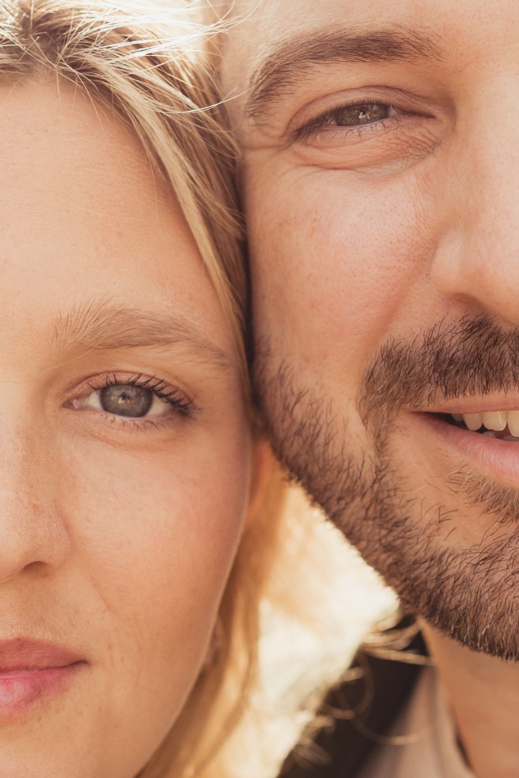 Close-up portrait of a smiling couple with blonde woman and bearded man cheek to cheek outdoors.