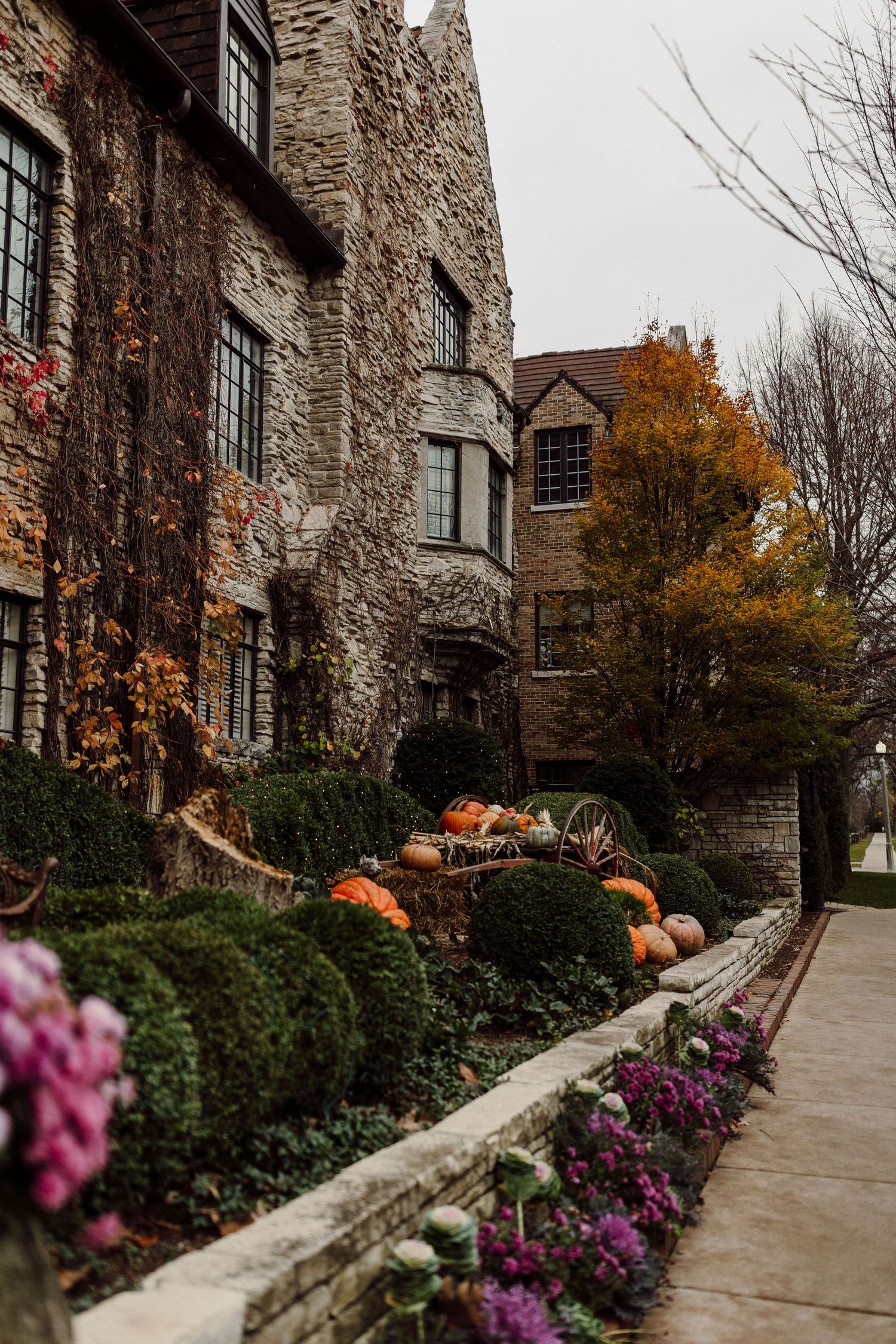Stone manor house adorned with autumn pumpkins and colorful fall flowers along a garden pathway.