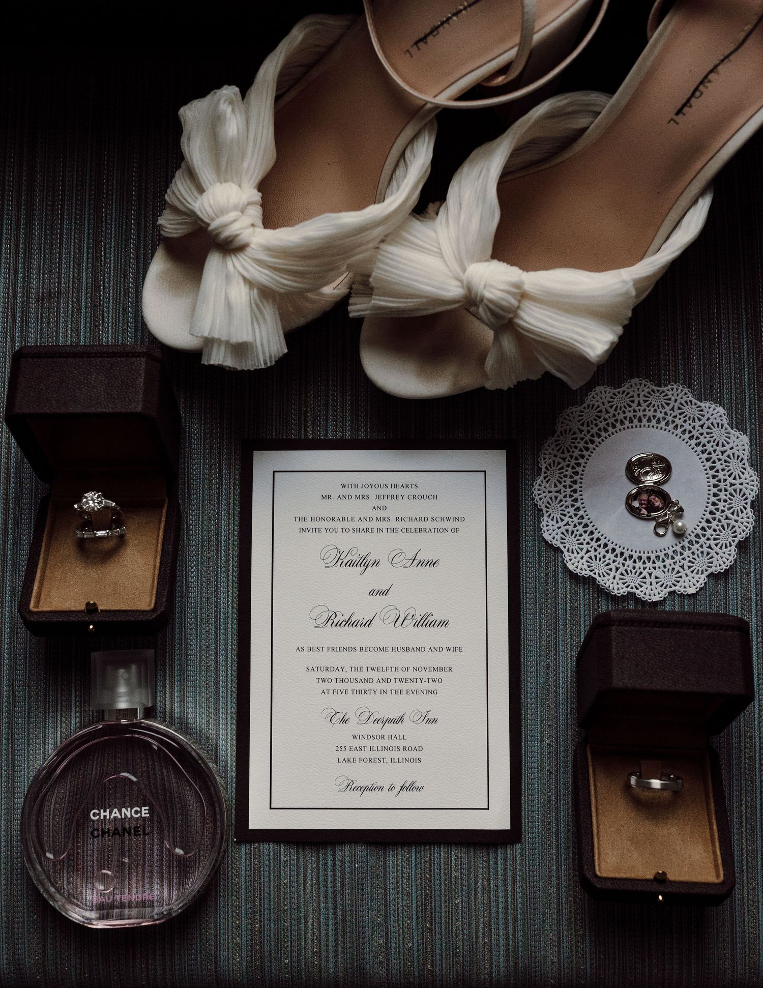 Elegant wedding flat lay featuring bridal heels, Chanel perfume, rings, and a formal wedding invitation.